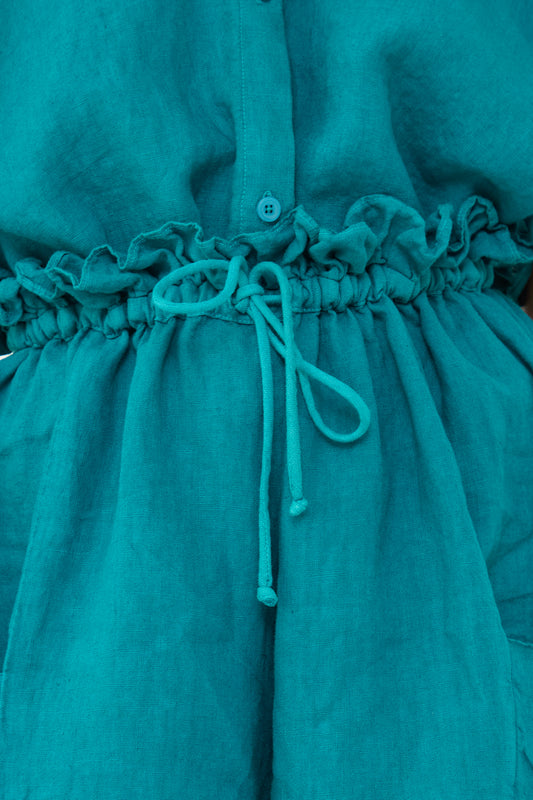 Close-up of a Peacock Linen Parachute Short by Black Crane with a buttoned front and gathered waist tied with a drawstring.