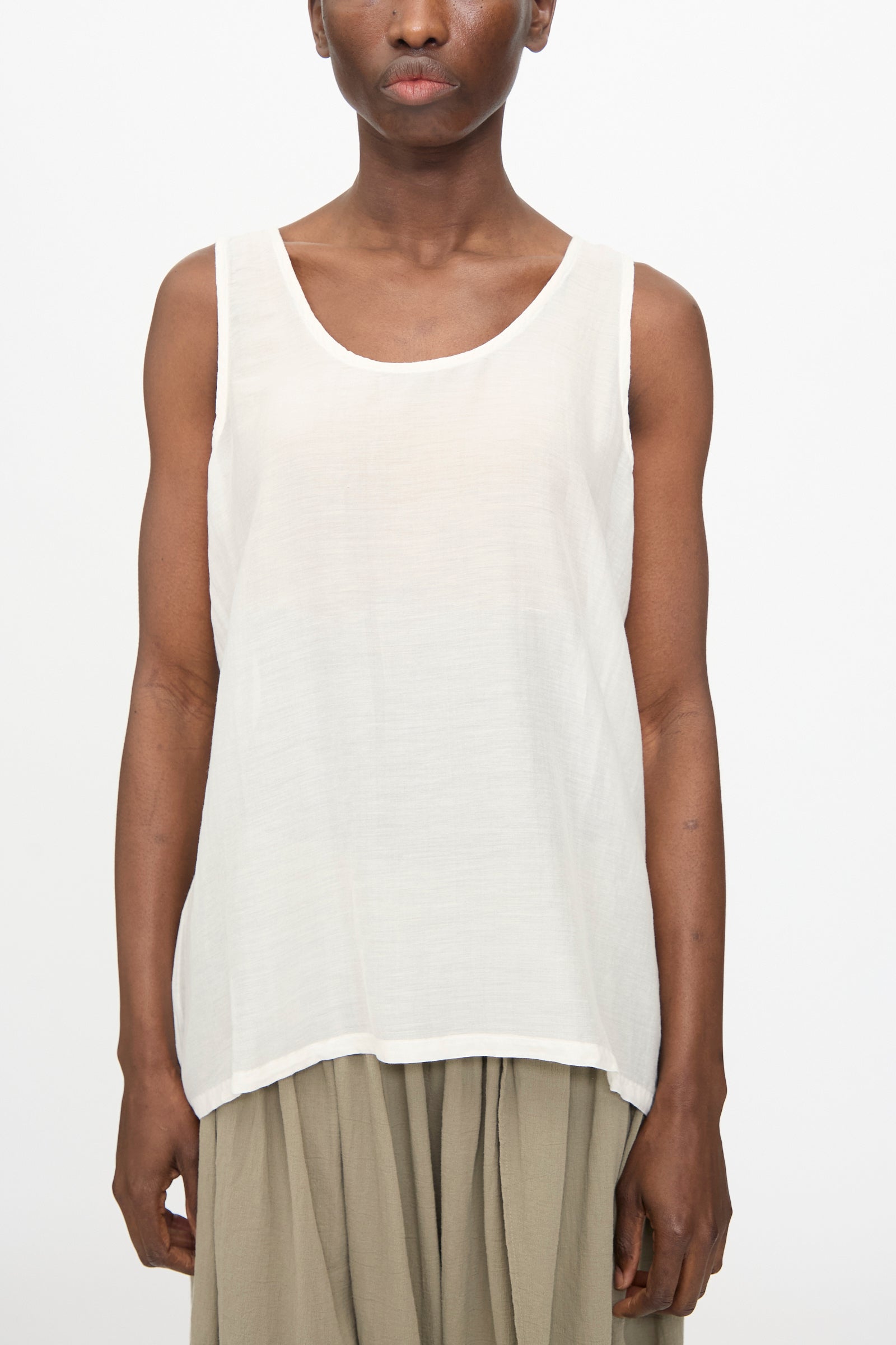 A person models the Black Crane Loose Tank Top in White, paired with beige pants, against a plain white background.