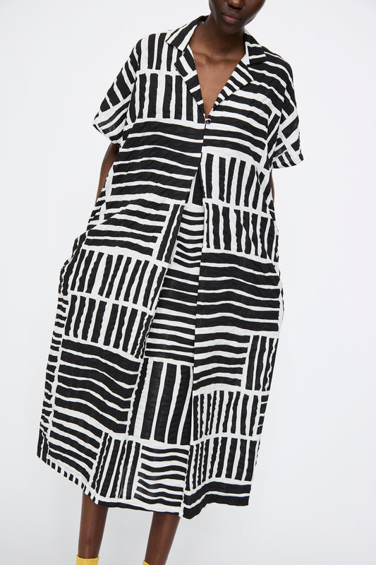 Made from soft Japanese cotton, the Black Crane Narrow Kite Dress in Black Print features a collared design with short sleeves and a mix of horizontal and vertical graphic stripes in black and white.