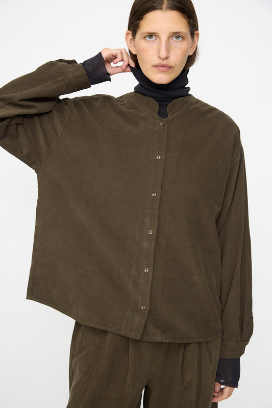 A person wearing the Black Crane Nehru Shirt in Dark Forest over a black turtleneck and brown pants stands against a plain white background.