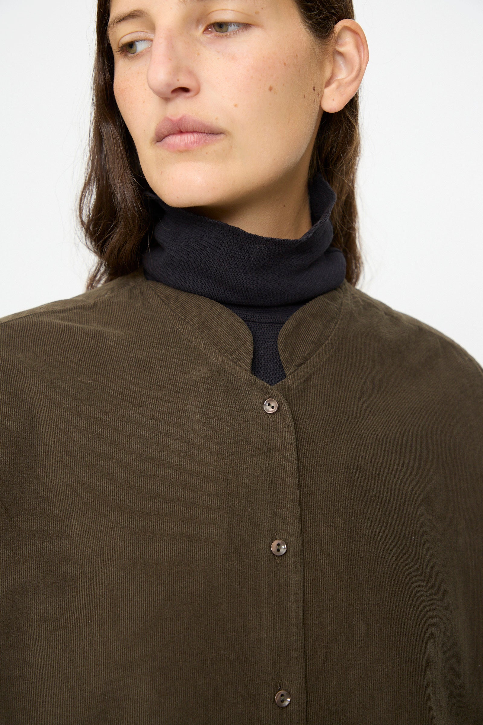 A person wears the Black Crane Nehru Shirt in Dark Forest over a black turtleneck, gazing slightly to the side against a plain background.