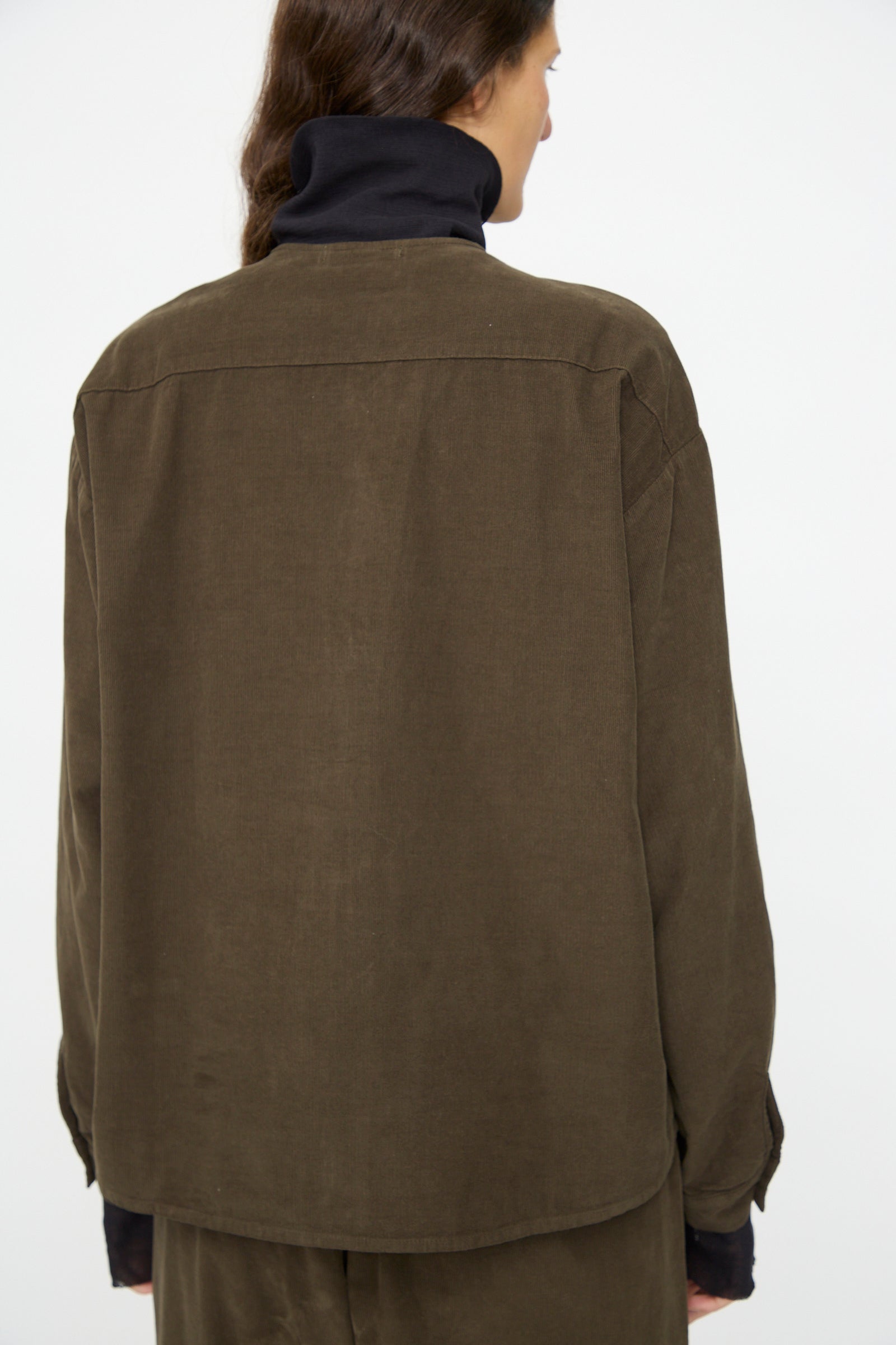 A person is seen from the back wearing the Black Crane Nehru Shirt in Dark Forest over a black turtleneck, set against a plain light background.