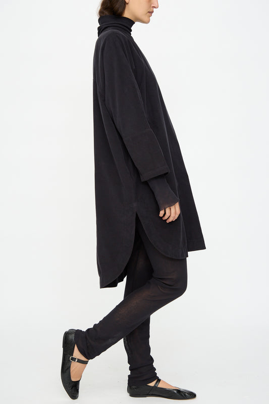 A person in the Black Crane Painter Dress in Dark Navy, paired with black leggings and ballet flats, stands sideways against a plain white background.
