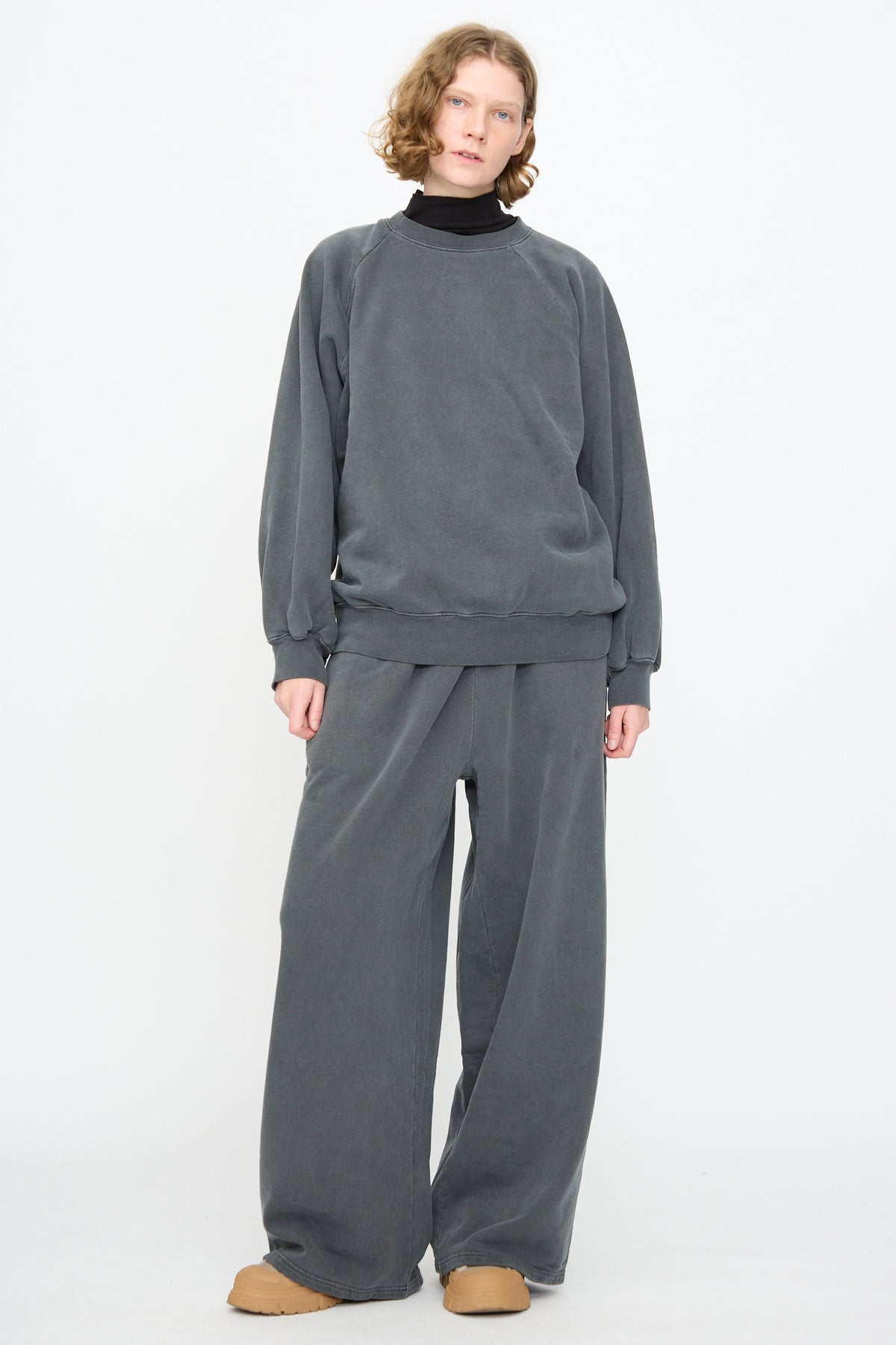 A person wearing the Black Crane Raglan Sweatshirt in Indigo, styled with matching wide-leg pants and tan shoes, stands against a plain white background.