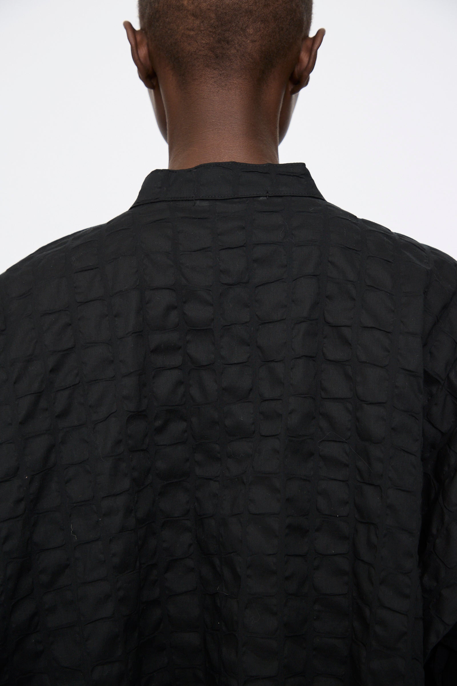 Close-up of the back of a person wearing the Black Crane Ripple Finish Shirt in Black, made from Japanese cotton with a subtle textured grid pattern.