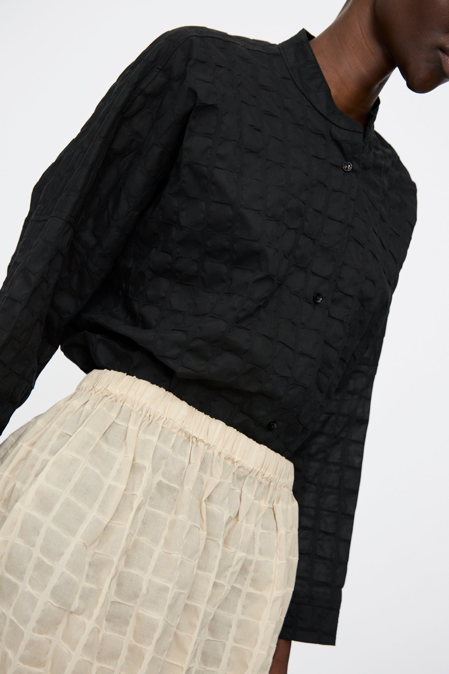 A person wearing a textured black button-up shirt with a collar and the Black Crane Ripple Finish Skirt in Beige, a high-waisted Japanese cotton midi skirt.