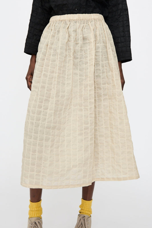 A person wears the Black Crane Ripple Finish Skirt in Beige, paired with yellow socks, taupe shoes, and a black top.