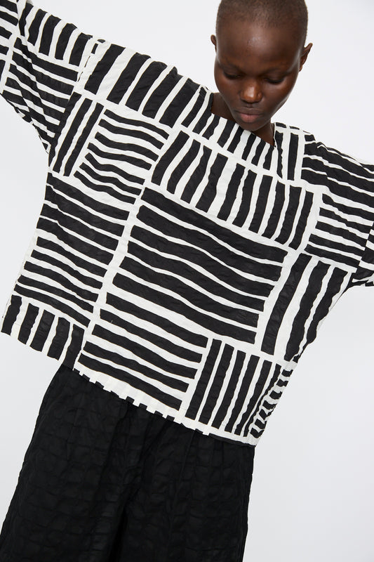 A person wears the Black Crane Short Sleeve Square Neck Top in Black Print with black textured trousers, standing against a plain background.