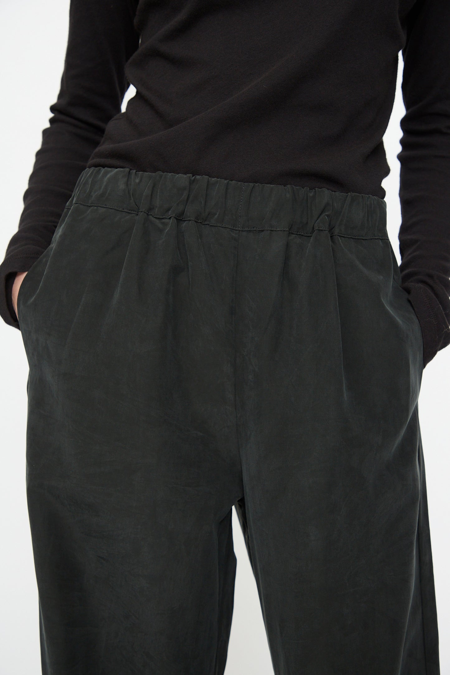 Model wearing the Black Crane Straight Pants in Black—loose, relaxed fit straight pants crafted from a soft cotton cupro blend—paired with a long-sleeve black top, shown from shoulder to thigh with hands in pockets.