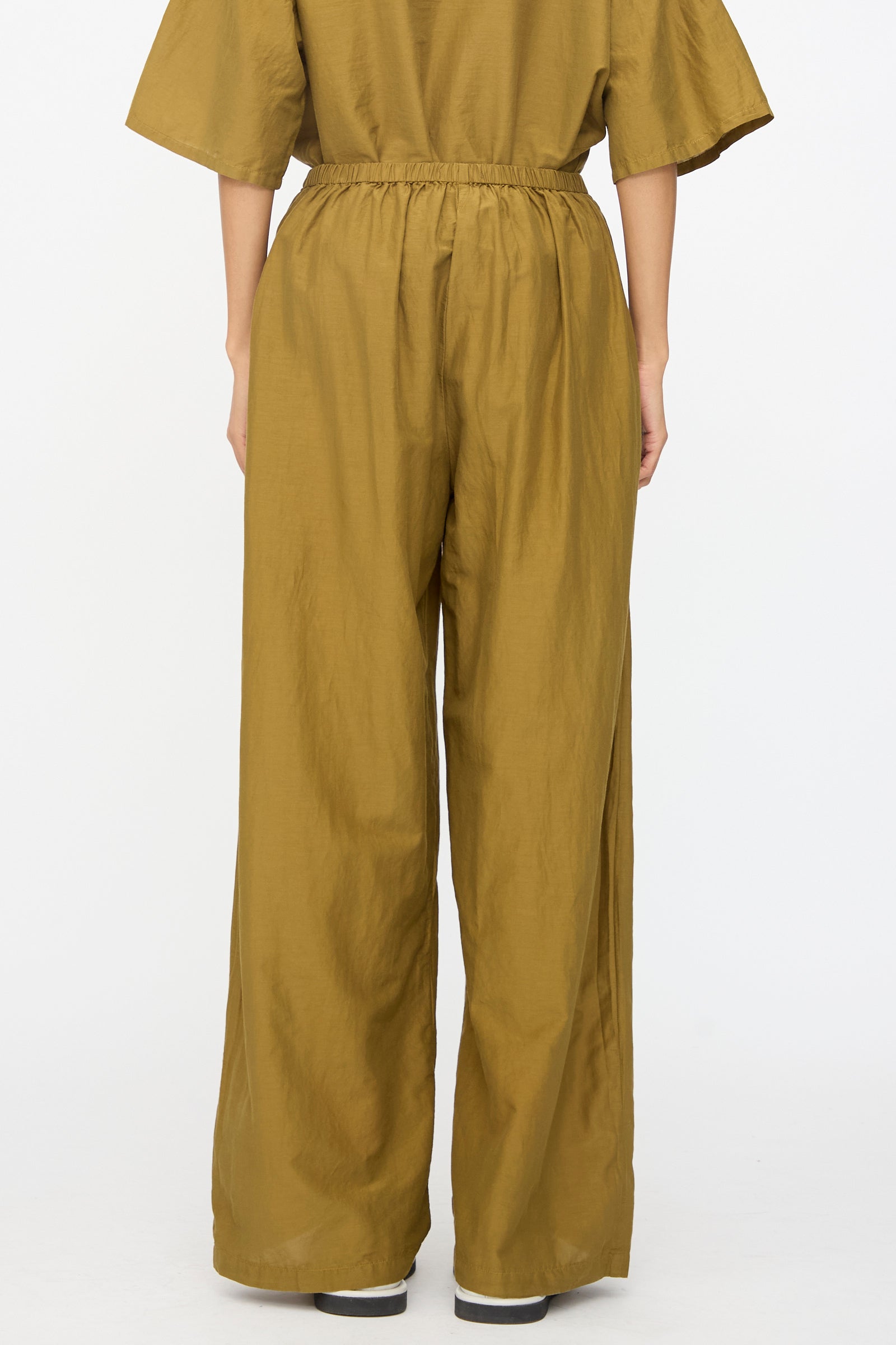 A person is seen from the back wearing Black Crane’s Straight Pants in Dark Olive with a relaxed fit, styled with a matching top, set against a plain white background.