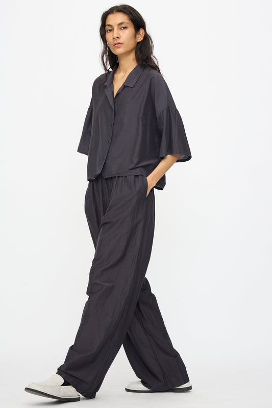 Person wearing Black Crane Straight Pants in Faded Black with a relaxed fit, dark gray button-up shirt and white slip-on shoes, walking against a plain white background.