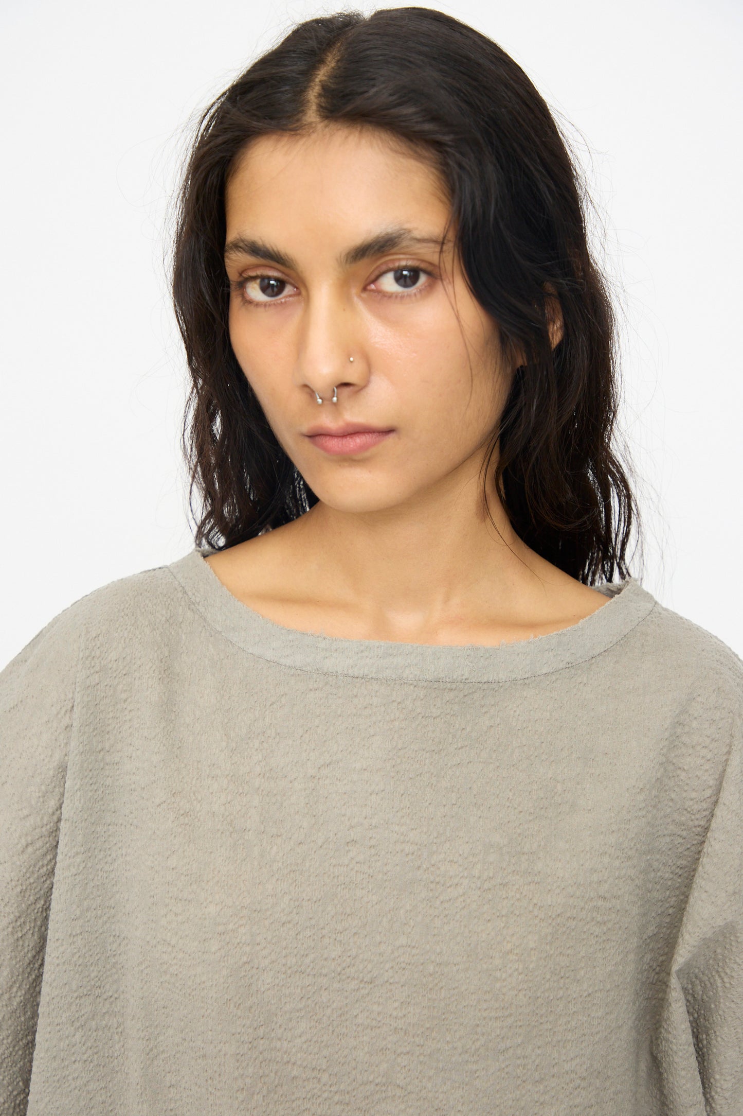 A person with long dark hair and a nose ring wears the Black Crane Textured Cotton Boxed Top in Pale Grey, looking directly at the camera against a plain background.