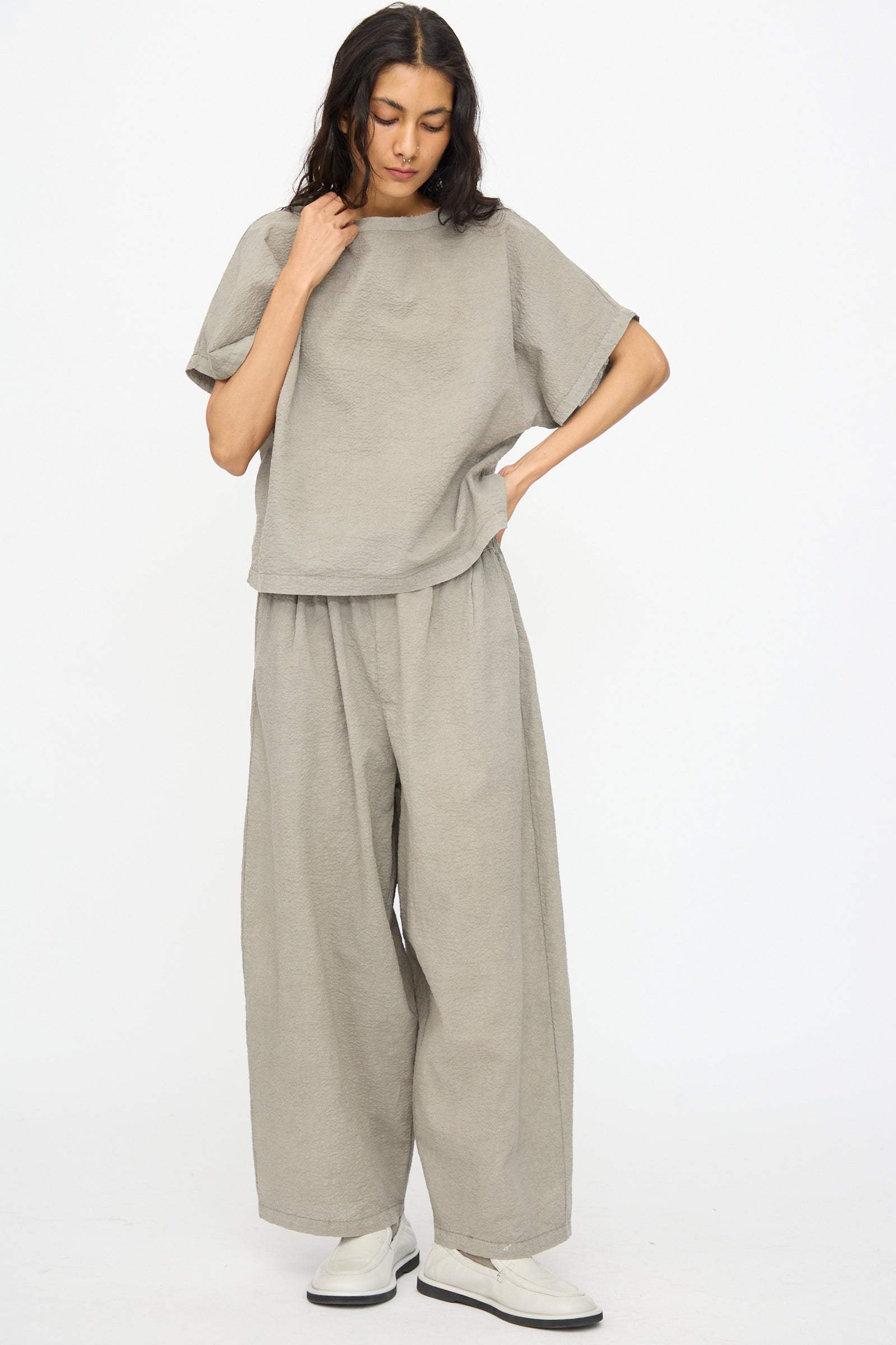A person wears the Black Crane Textured Cotton Boxed Top in Pale Grey with matching wide-leg pants and white shoes, standing against a plain white background.