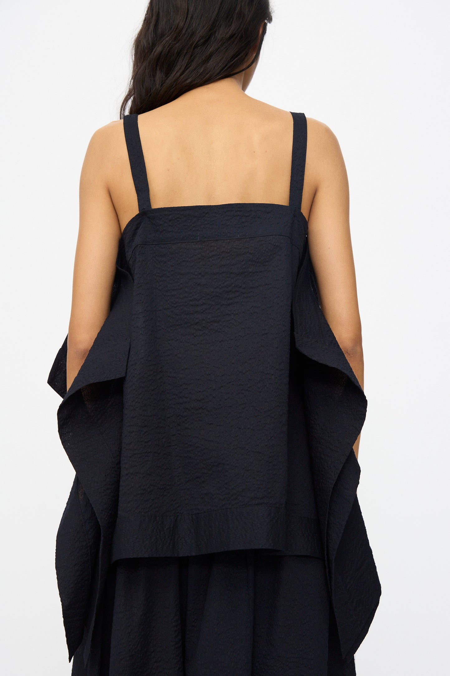A person with long dark hair wears the Black Crane Textured Cotton Paper Top in Midnight, featuring wide straps and a subtle square neckline, photographed from the back against a plain background.