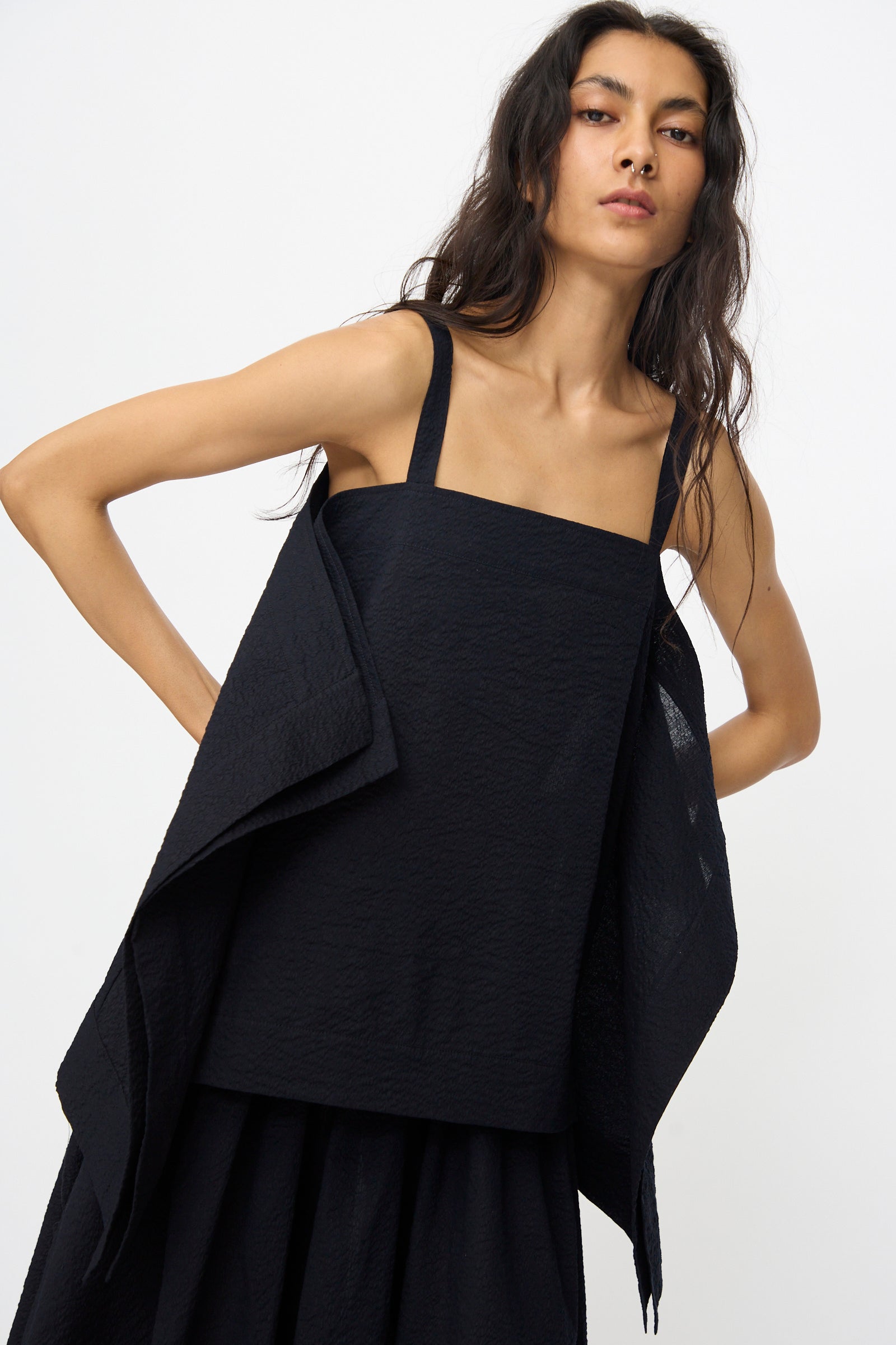 A woman with long dark hair wears the Black Crane Textured Cotton Paper Top in Midnight and a matching black skirt, standing against a plain white background.