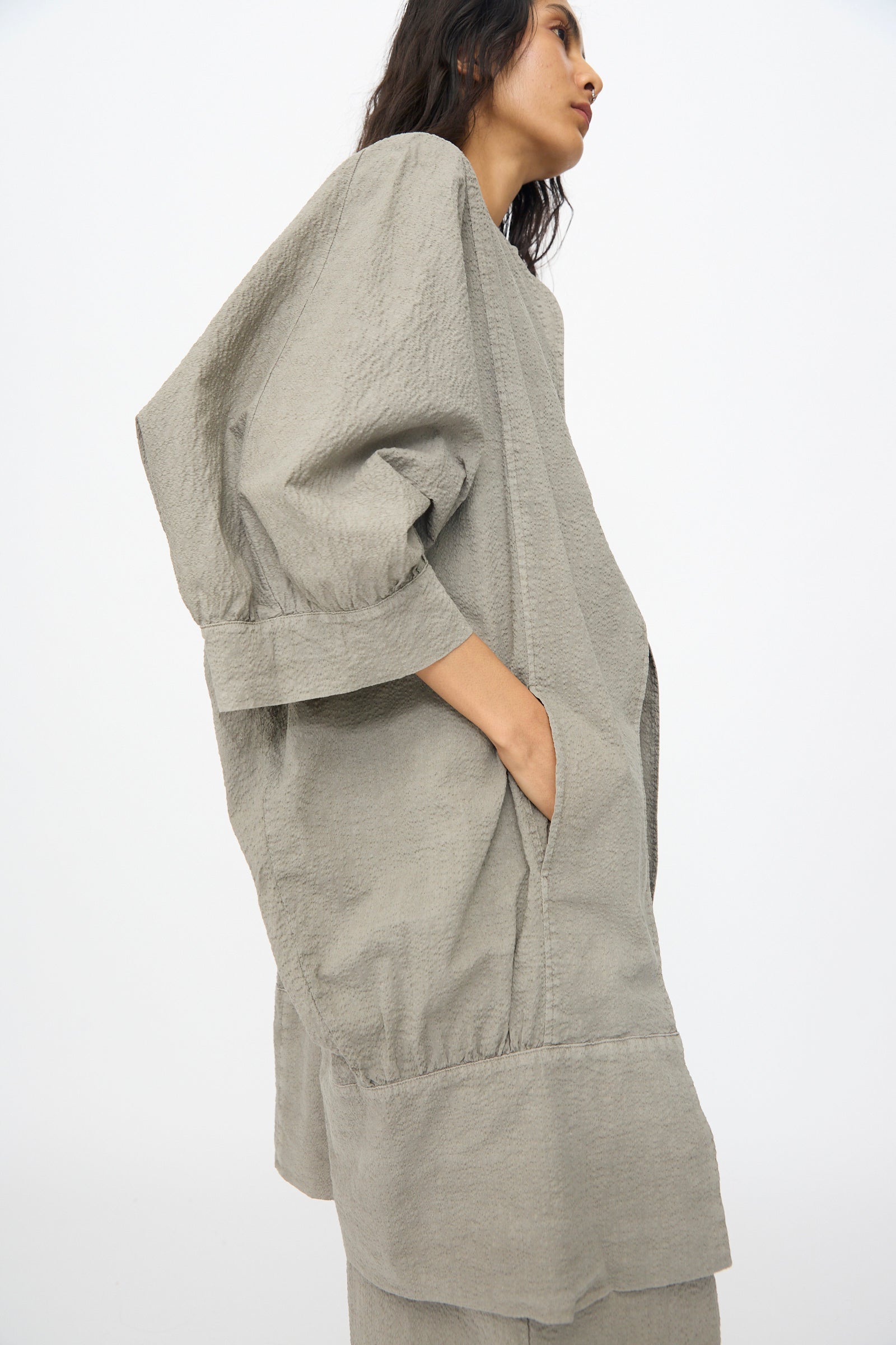 A person wears the Black Crane Textured Cotton Spoon Jacket in Pale Grey—an oversized, lightweight Japanese textured cotton jacket with wide sleeves and pockets—while standing against a plain white background.