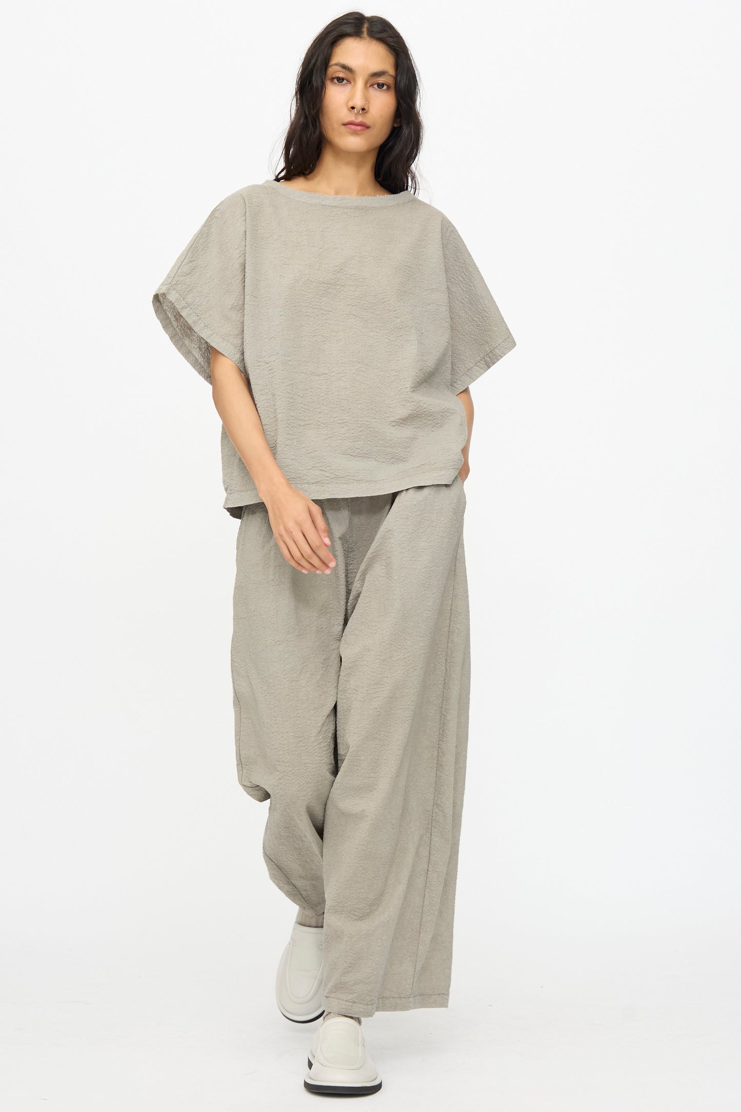 A person wears Black Crane’s Textured Cotton Wide Pants in Pale Grey with a matching loose top and white shoes, standing against a plain white background.