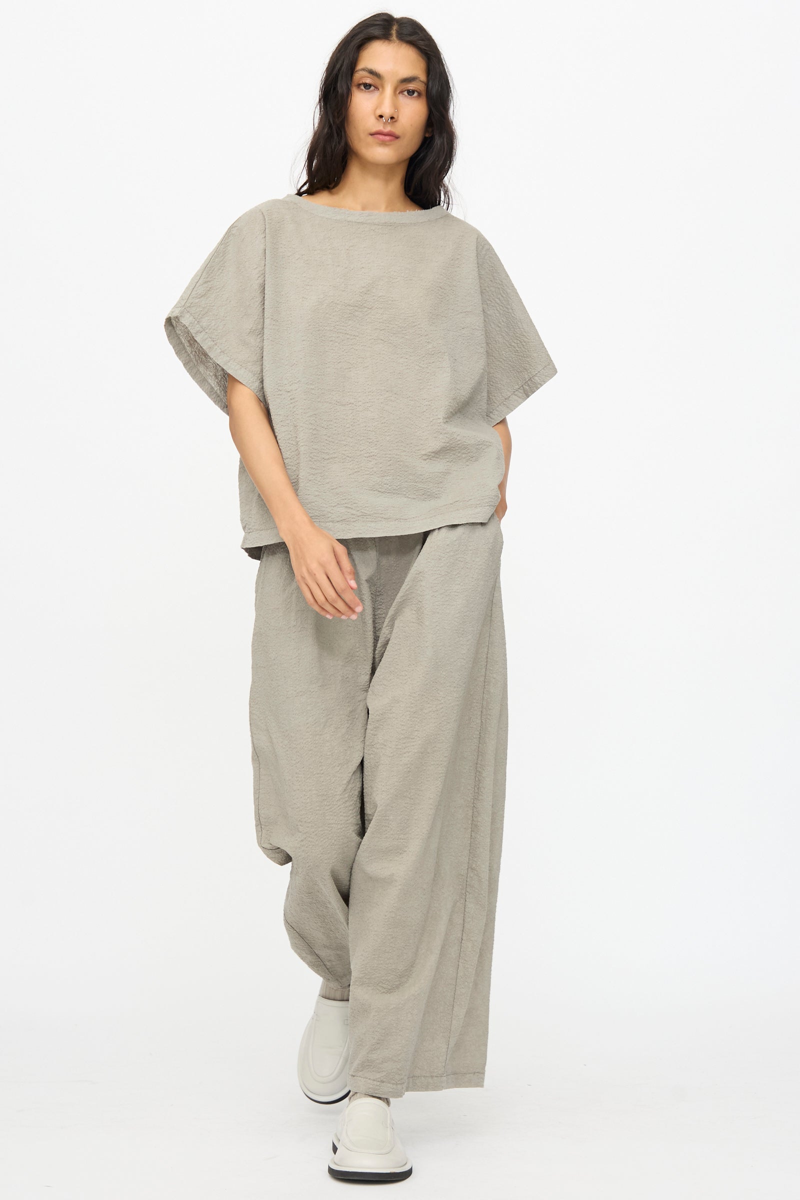 A person wears Black Crane’s Textured Cotton Wide Pants in Pale Grey with a matching loose top and white shoes, standing against a plain white background.