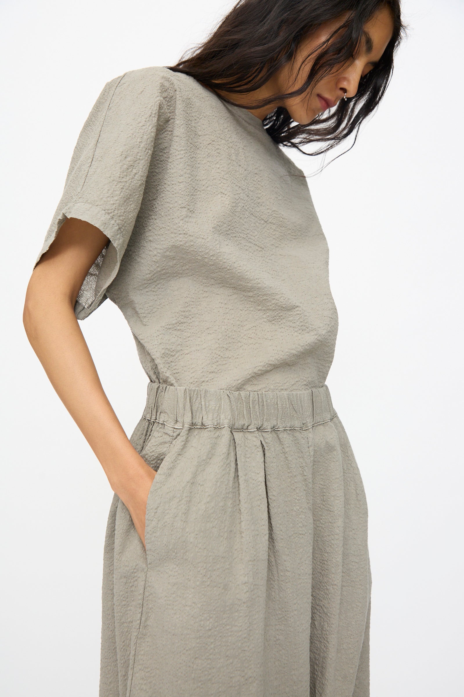 Person wearing Black Crane Textured Cotton Wide Pants in Pale Grey, paired with a loose short-sleeve top, hands in pockets, standing against a plain background.