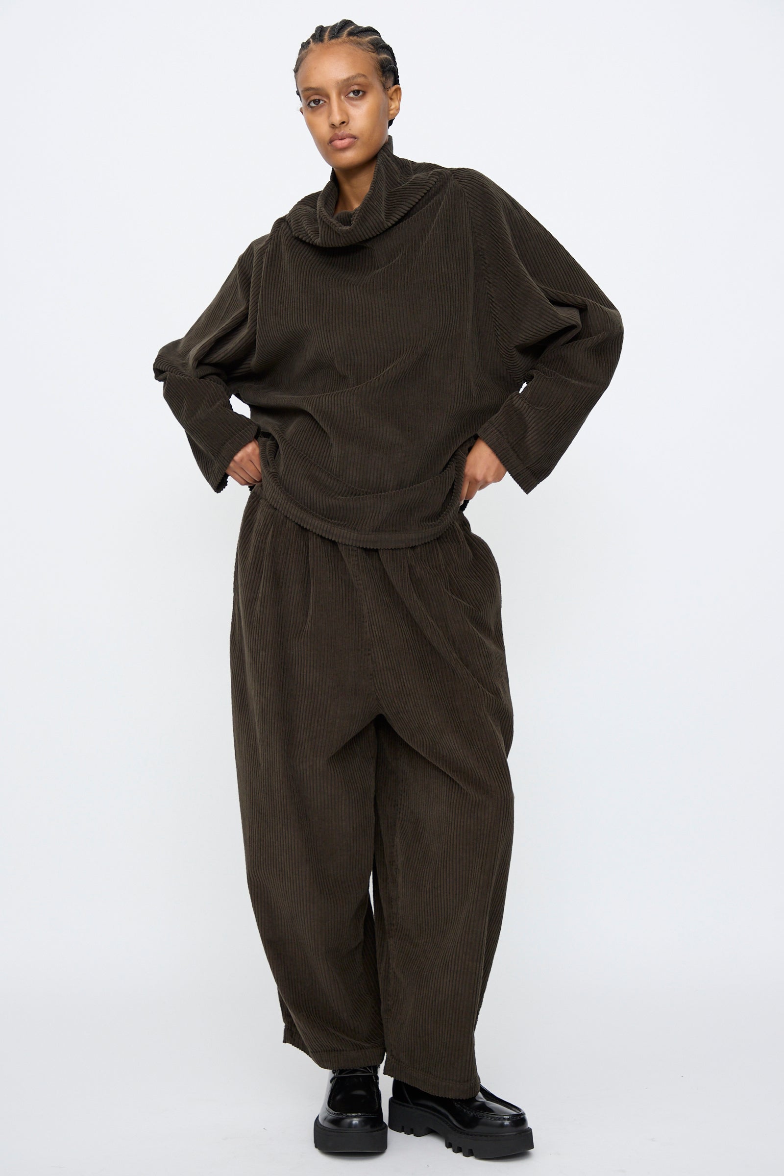 A person wears the Black Crane Tube Top in Forest, a loose-fitting cotton corduroy style, paired with matching wide-leg pants, standing against a plain white background.