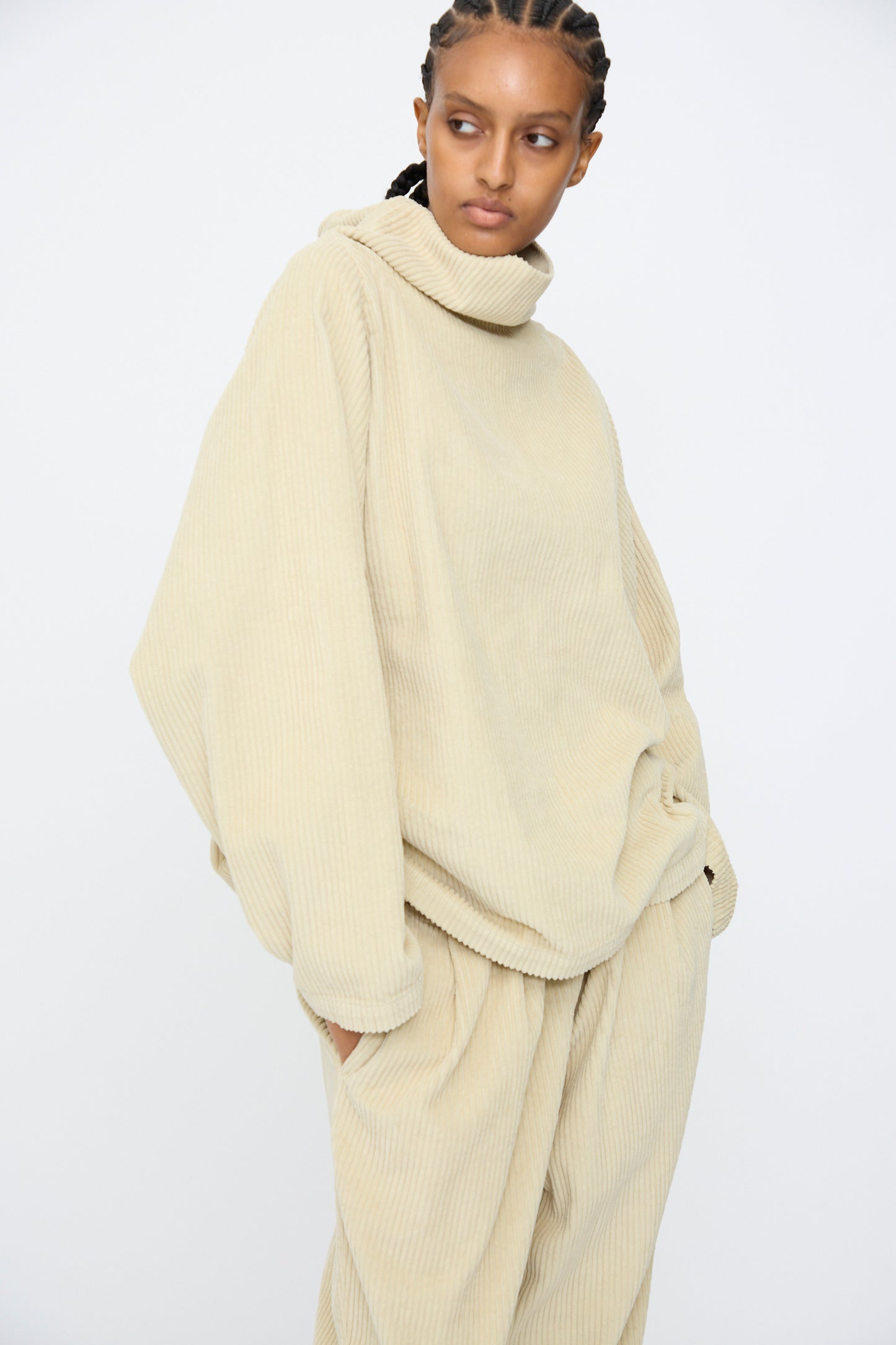 A person wearing the Black Crane Tube Top in Ivory, a loose-fitting cotton corduroy piece with a boxy silhouette, and matching pants stands against a plain white background.