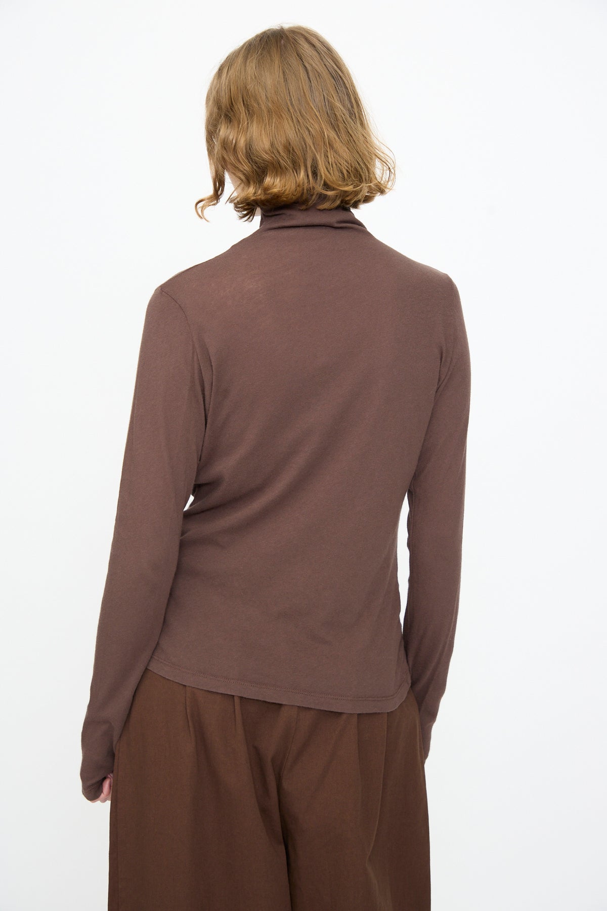 Person with short, light brown hair wearing a long-sleeve, relaxed fit Turtleneck in Dark Plum by Black Crane and matching dark plum pants, photographed from the back against a plain white background.