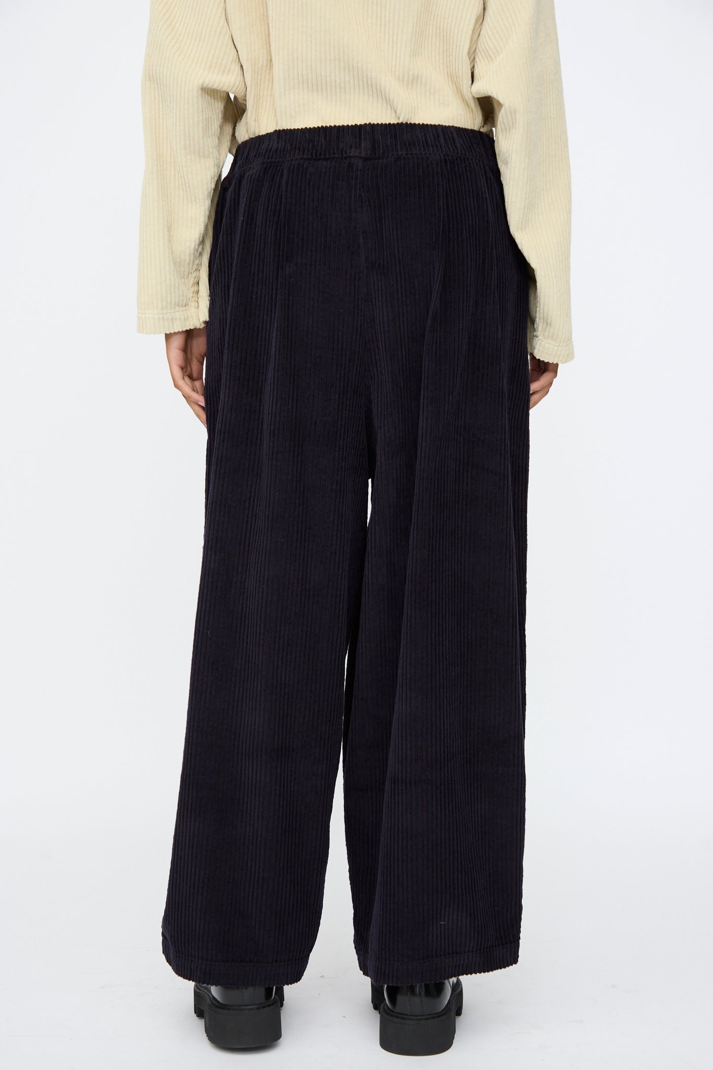 Person wearing a light beige long-sleeve top and Black Crane Wide Pants in Dark Navy with an elastic waist, standing with their back to the camera.
