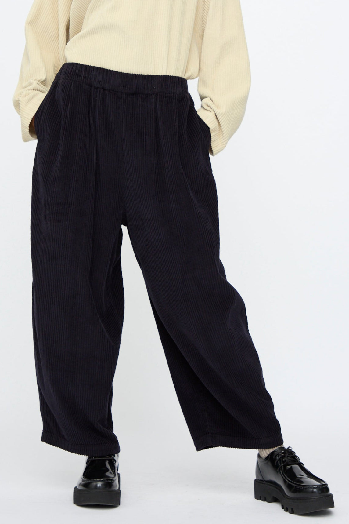 A person wears Black Crane's Wide Pants in Dark Navy, paired with a cream long-sleeve top and black platform shoes, standing against a plain background.