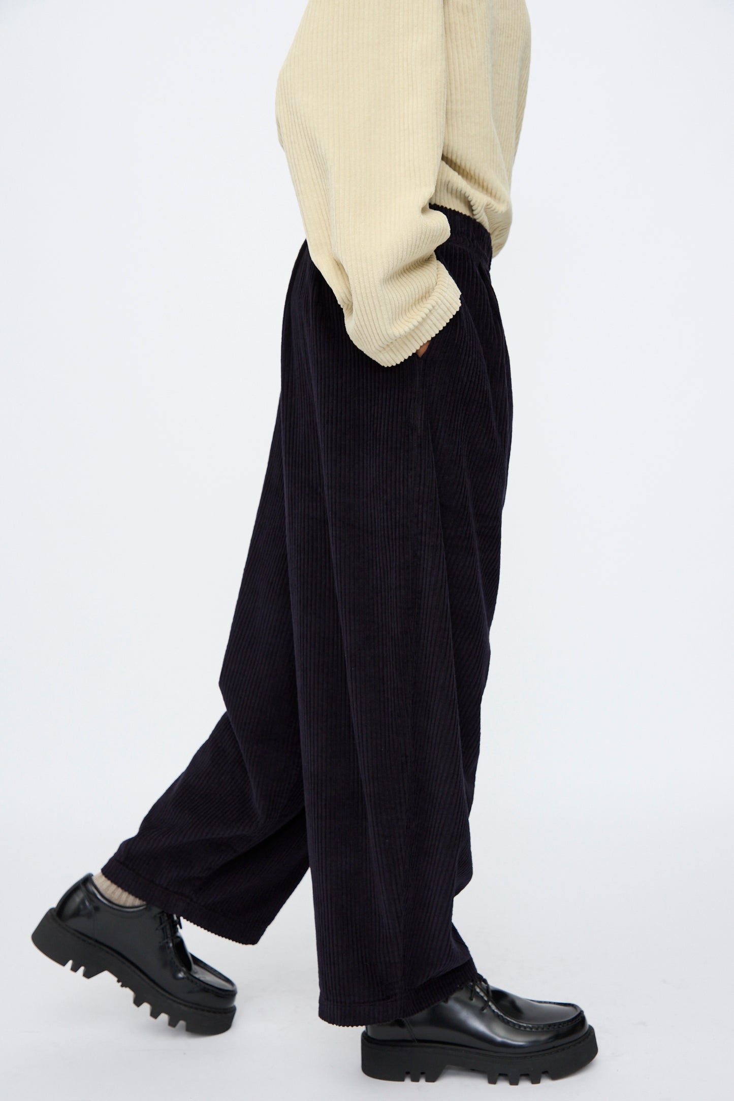 A person is wearing Black Crane's Wide Pants in Dark Navy with a light beige sweater, light socks, and black chunky shoes, walking against a plain white background.