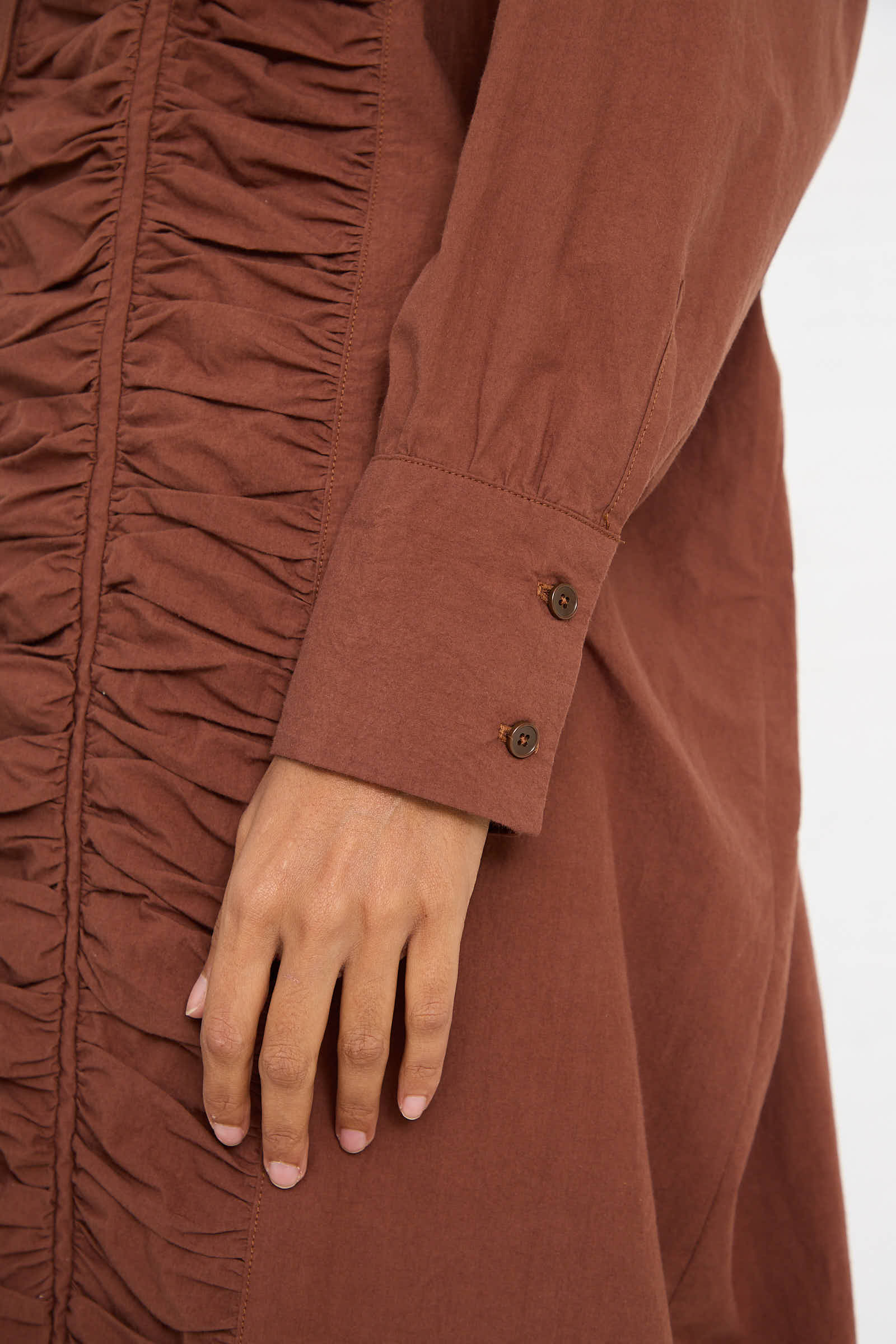 Close-up of a person’s hand touching the side of the Woven Cotton Ruffled Dress in Cacao by Black Crane, showcasing the ruched detailing and buttoned cuffs, which highlight the relaxed fit of this midi dress crafted from soft Japanese cotton.