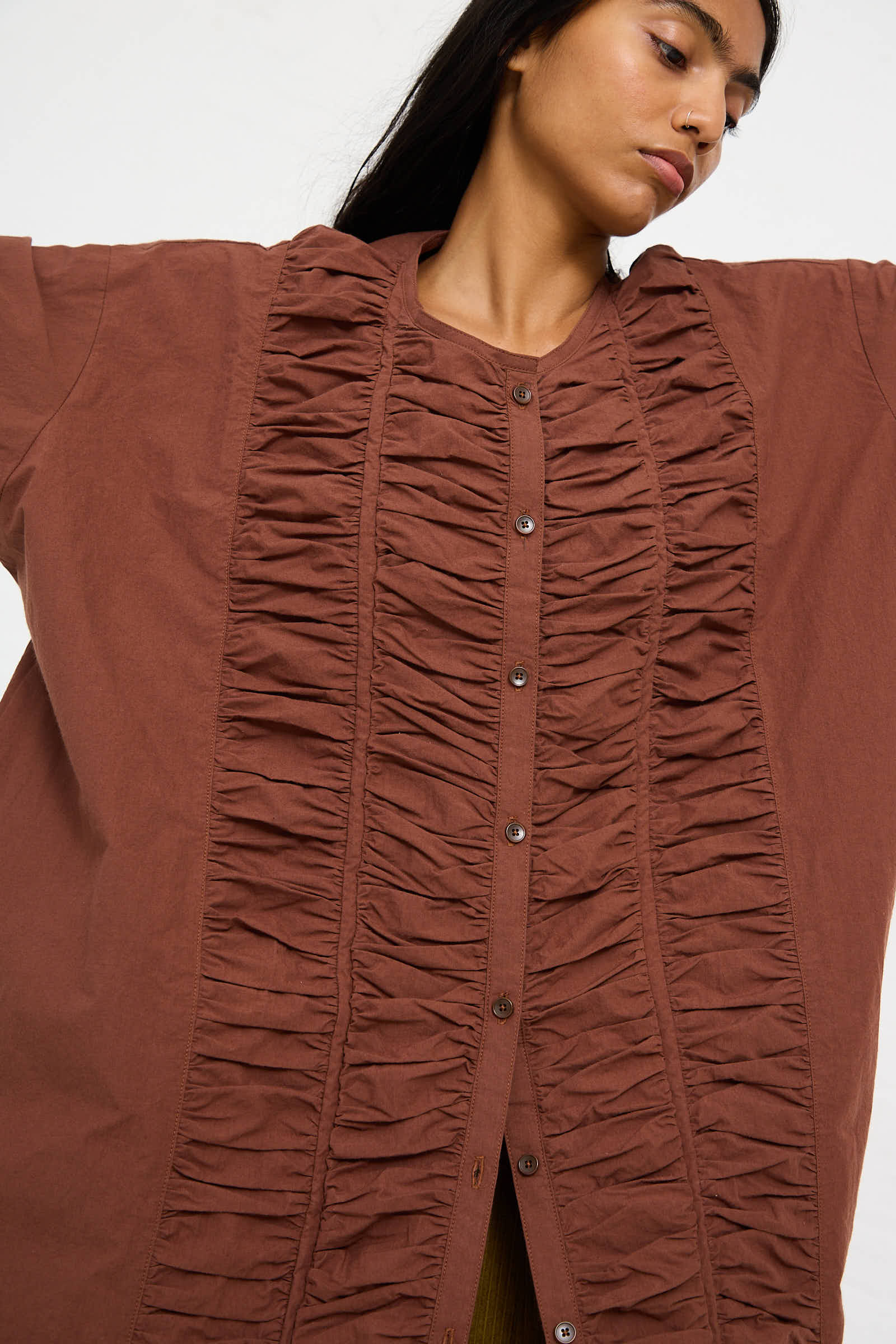 A person wearing the Woven Cotton Ruffled Dress in Cacao by Black Crane, handcrafted from Japanese cotton, stands with their arms outstretched.