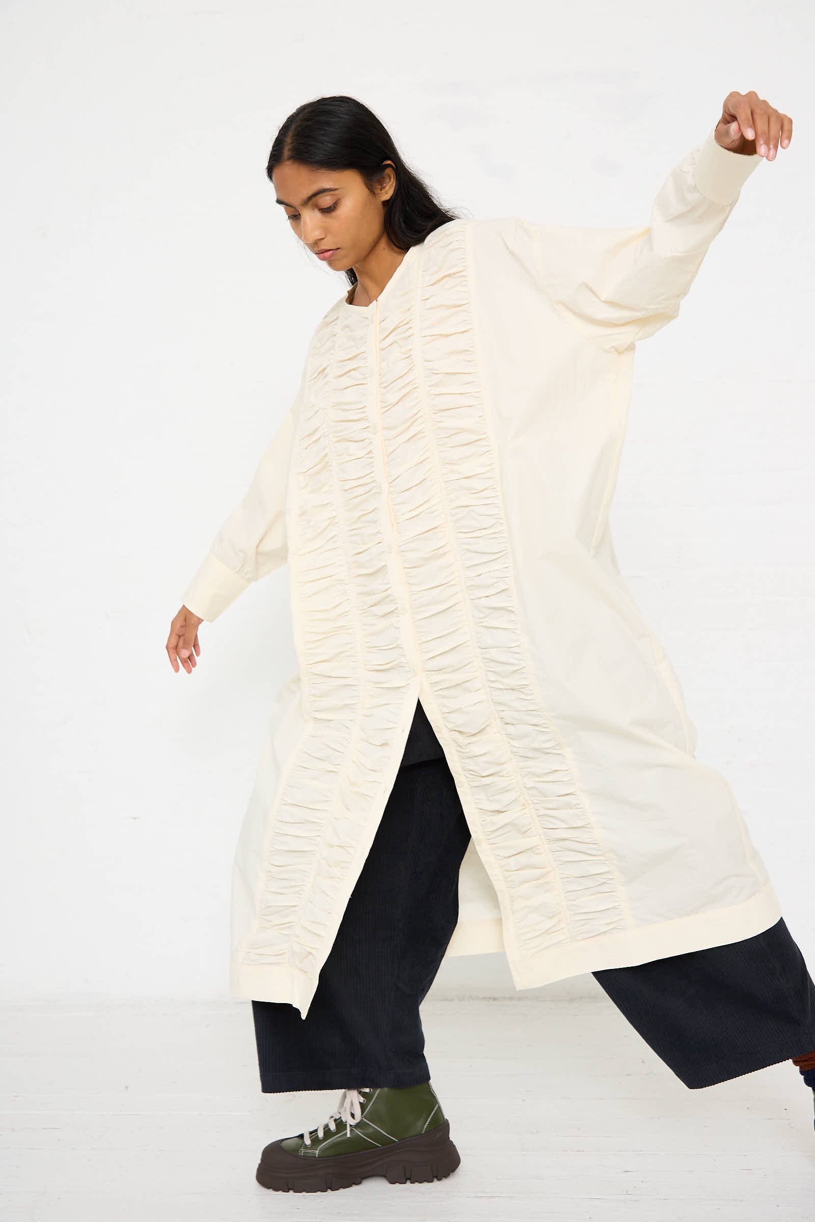 A person wearing the Black Crane Woven Cotton Ruffled Dress in Ivory stands with arms slightly outstretched. They have dark hair and are posing against a plain white background.