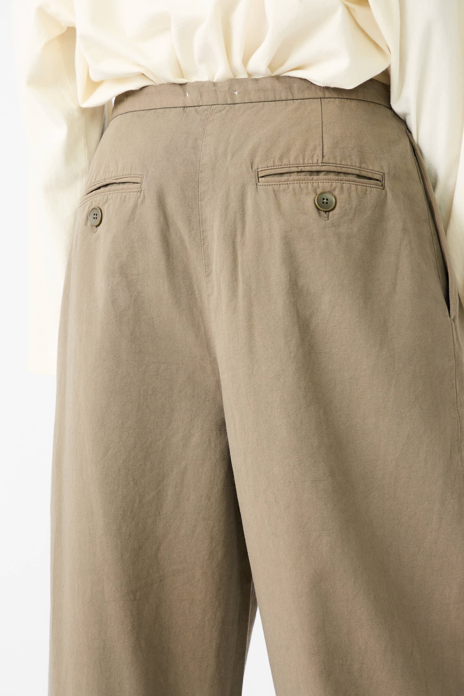 A person is wearing a white shirt and the Woven Cotton Straight Trouser in Dark Olive by Black Crane, seen from the back. The straight leg trousers, made from Japanese cotton, feature two rear buttoned pockets.