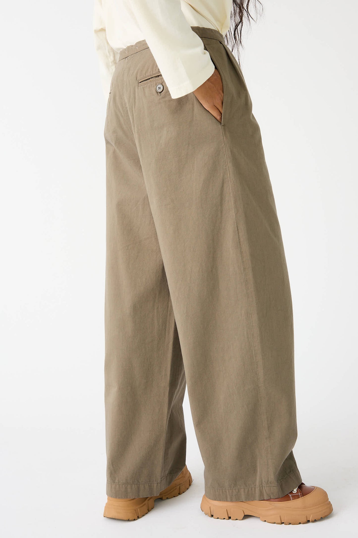 Individual wearing the Woven Cotton Straight Trouser in Dark Olive by Black Crane paired with brown shoes, captured from the side against a minimalist backdrop.