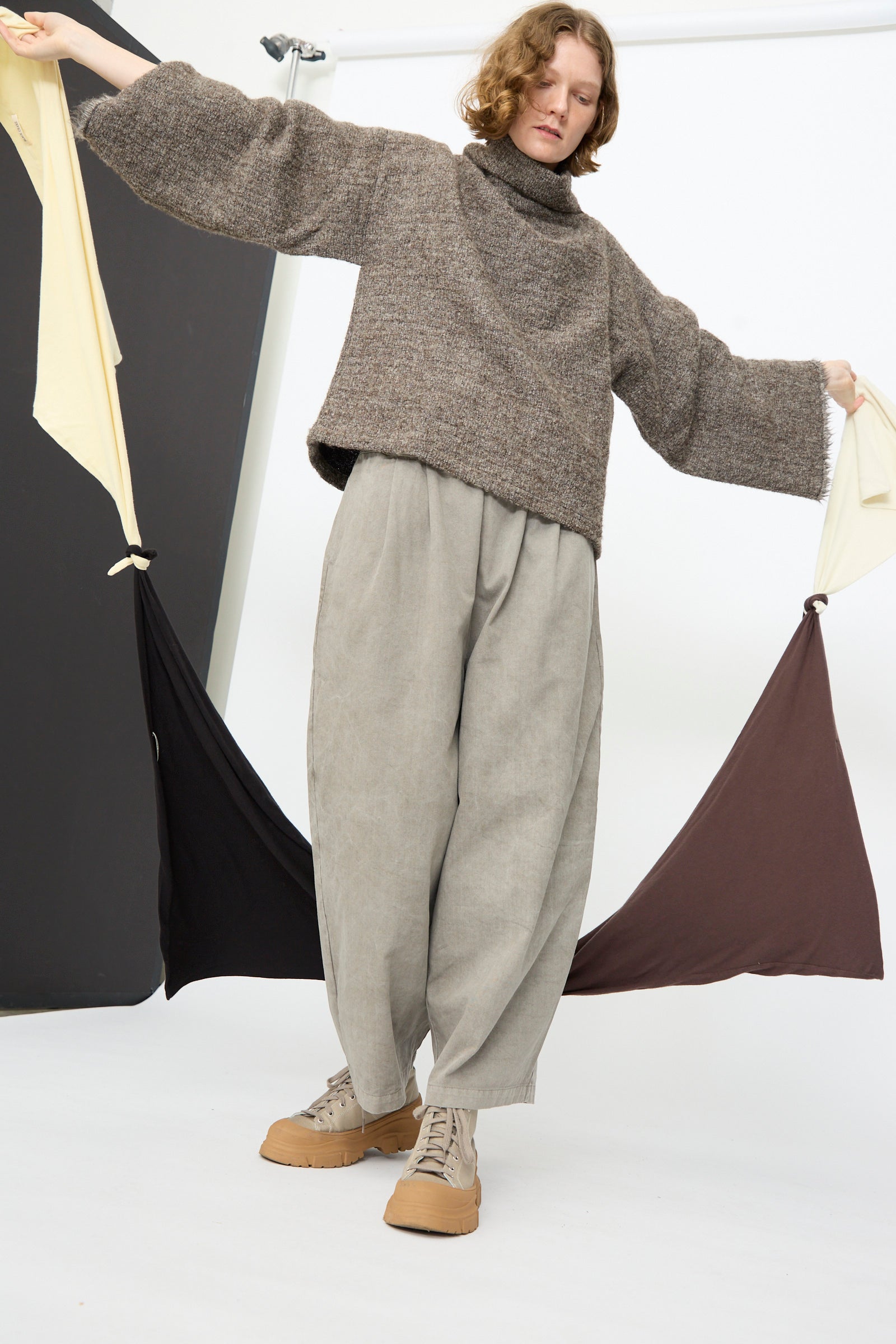 A model stands in a studio wearing Black Crane's Tube Top, and Wide Leg pant, holding up four scarves tied together.