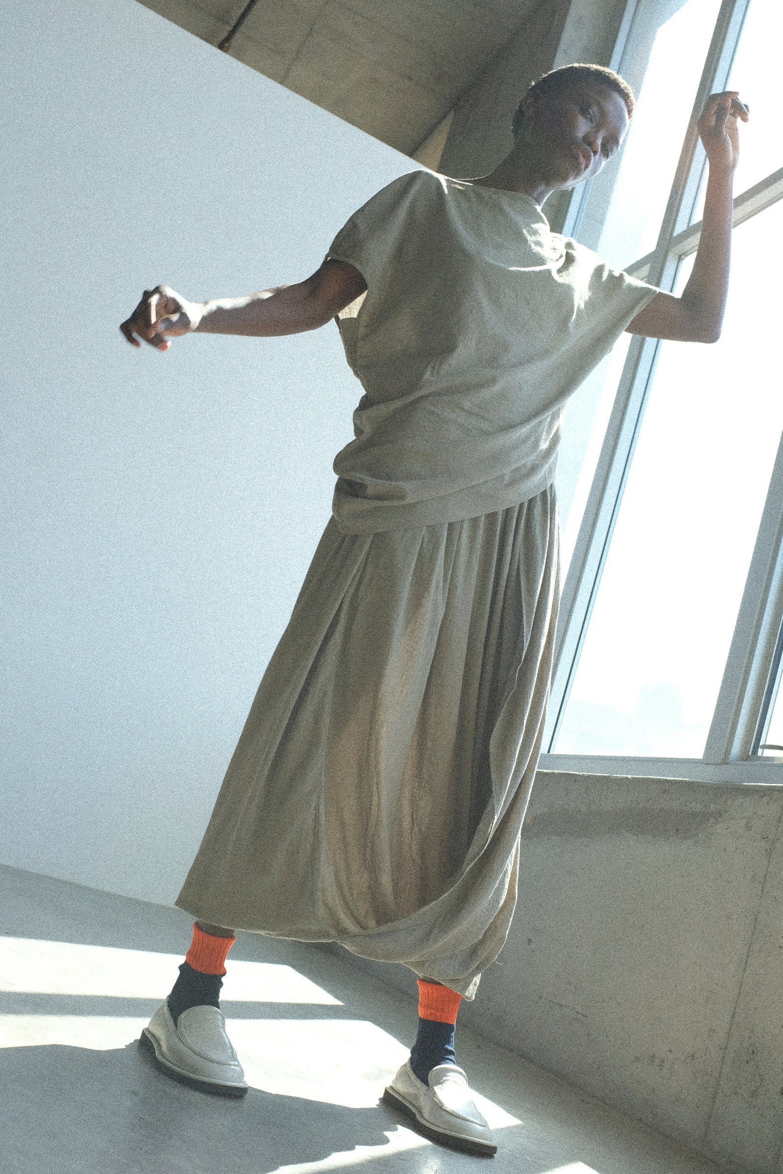 Person wearing Black Crane's Asymmetric Top in Cement with the Greek Column Skirt in Cement in a bright room with large windows.