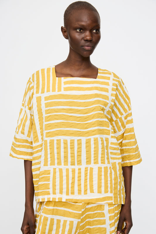A person wears the Black Crane Short Sleeve Square Neck Top in Gold Print, featuring a boxy fit and made from soft Japanese cotton, with matching pants, against a plain white background.