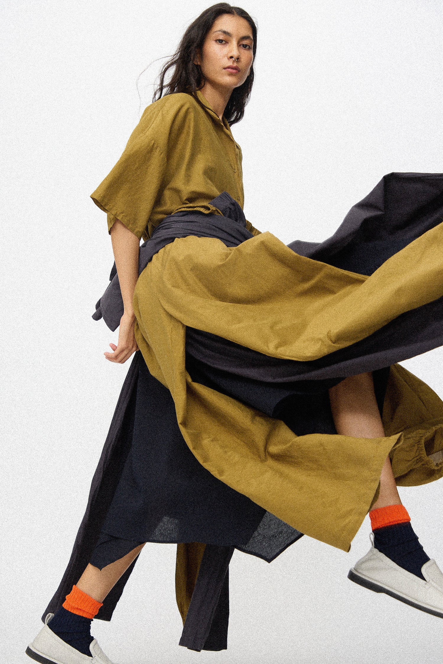 Woman wearing a pieces of Black Cranes SS26 collection tied around her waist, with orange socks and white sneakers on a white background.