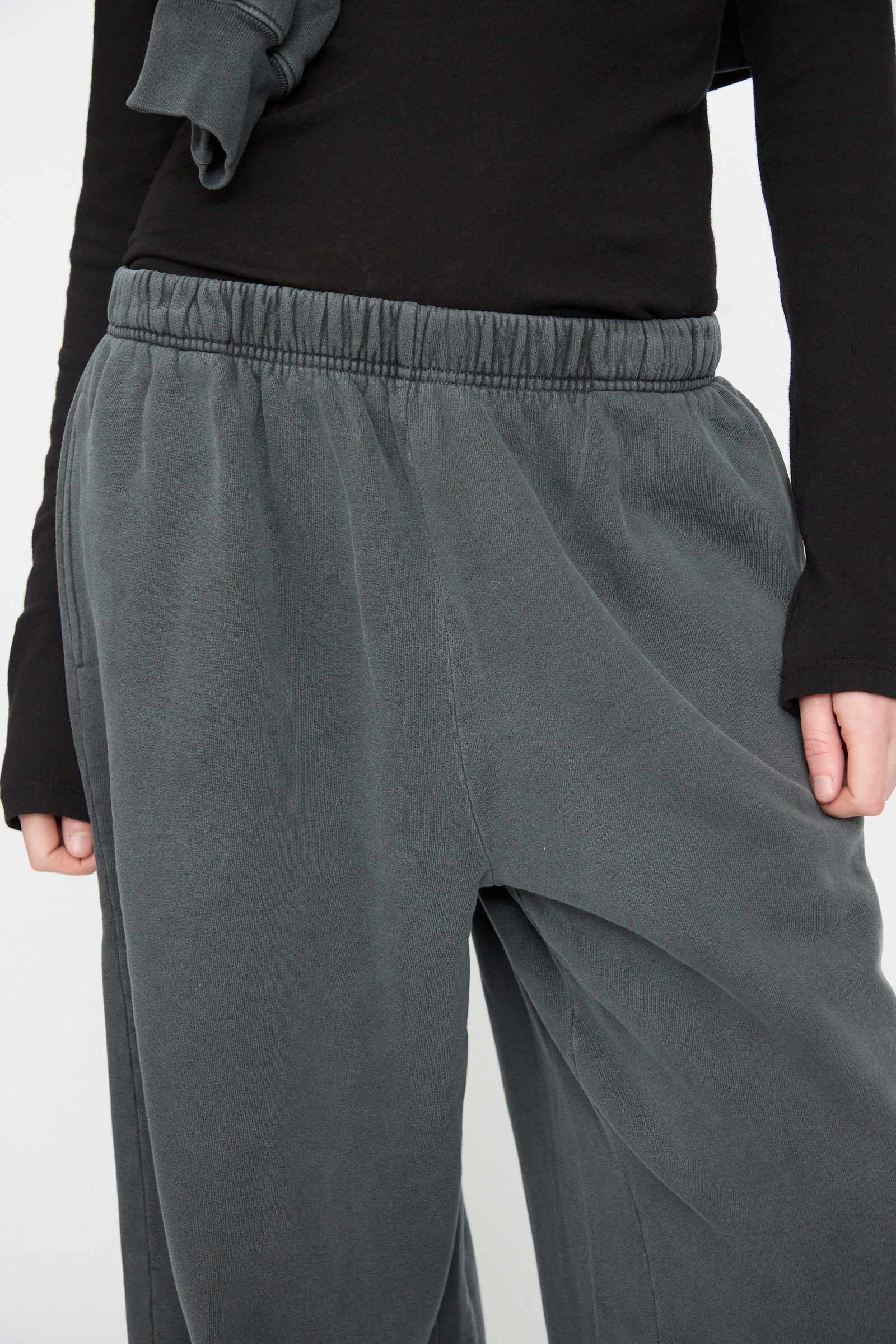A person wearing Black Crane’s Wide Long Sweatpants in Indigo and a black long-sleeve shirt, shown from the waist to mid-thigh against a plain background.