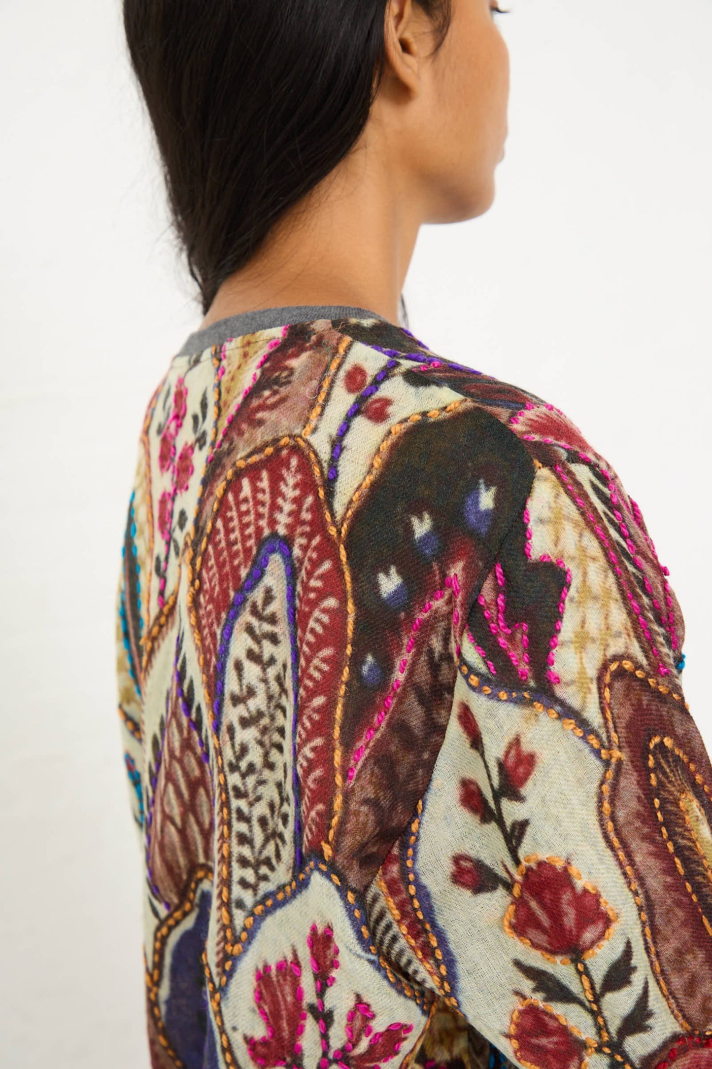 A person with long dark hair, turned away from the camera, is wearing the Bless Embroidered Wool No. 78 Sweater in Multicolor Brown, adorned with intricate floral motif embroidery and a blend of floral and abstract designs.