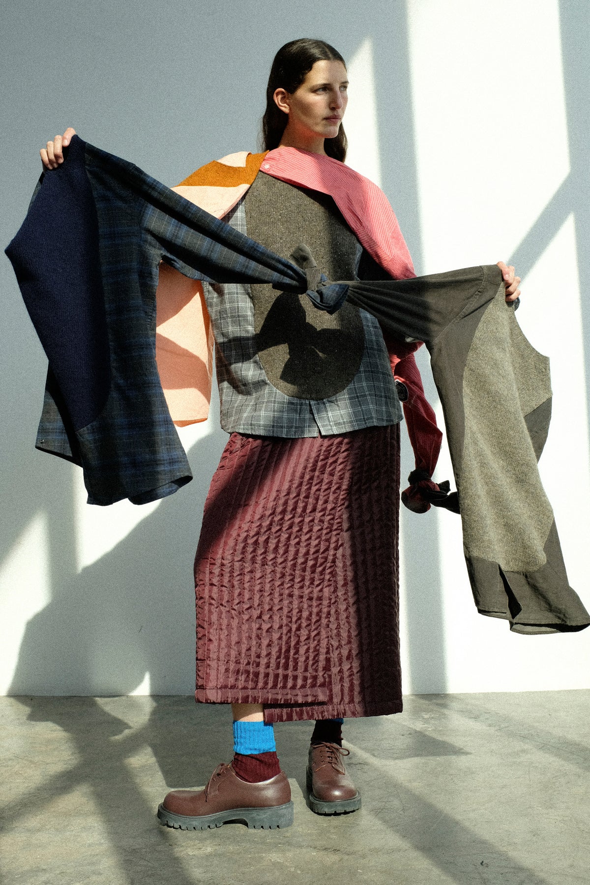 A woman in a sunlit studio with Bless's Frontinstertpullover around her shoulders, wearing the No. 08 Monpe Skirt in Burgundy.