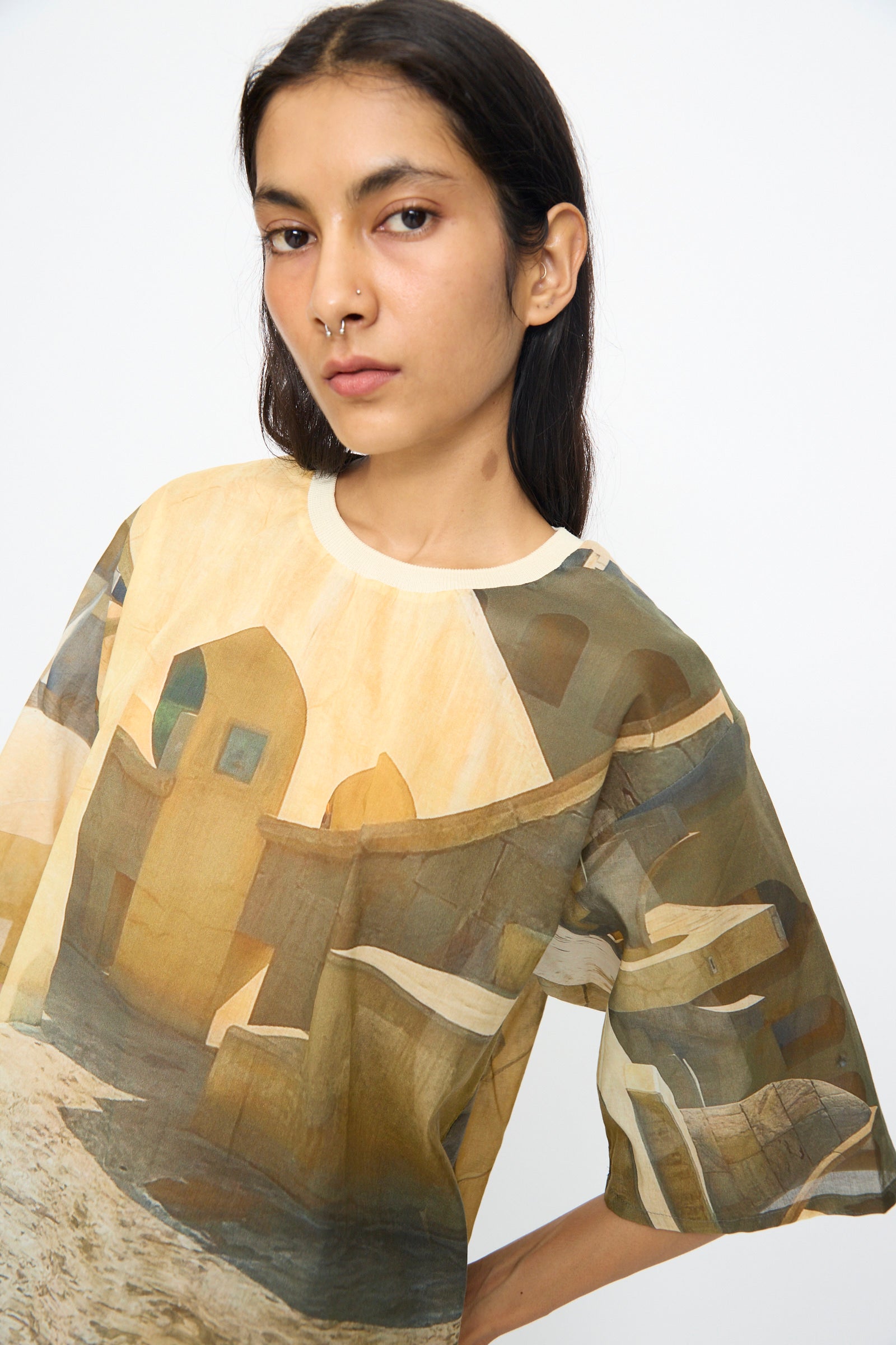 A person with long dark hair wears the Bless Holidayjaipurobservatory Tee in Print—an oversized, semi-sheer cotton top with an abstract architectural design—standing against a plain white background.