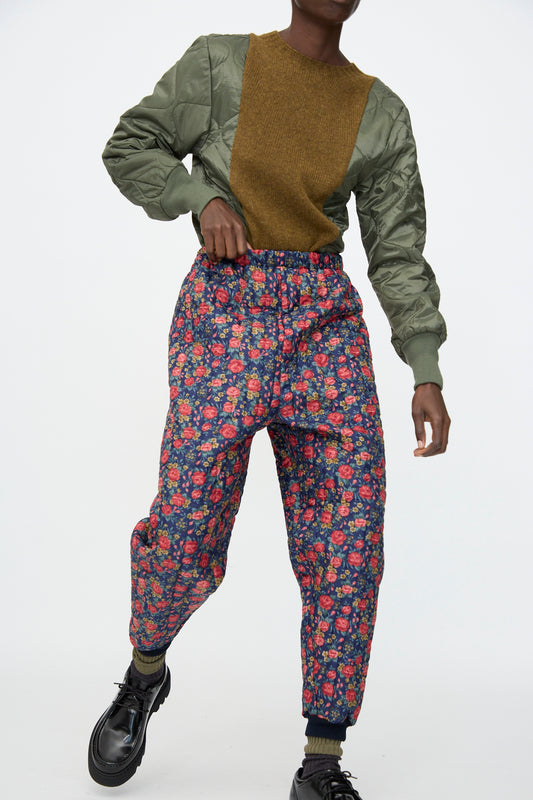 A person wears a green bomber jacket with a brown front panel, Bless No. 08 Monpe Pant in Floral Print I, and black shoes, posed against a plain white background.