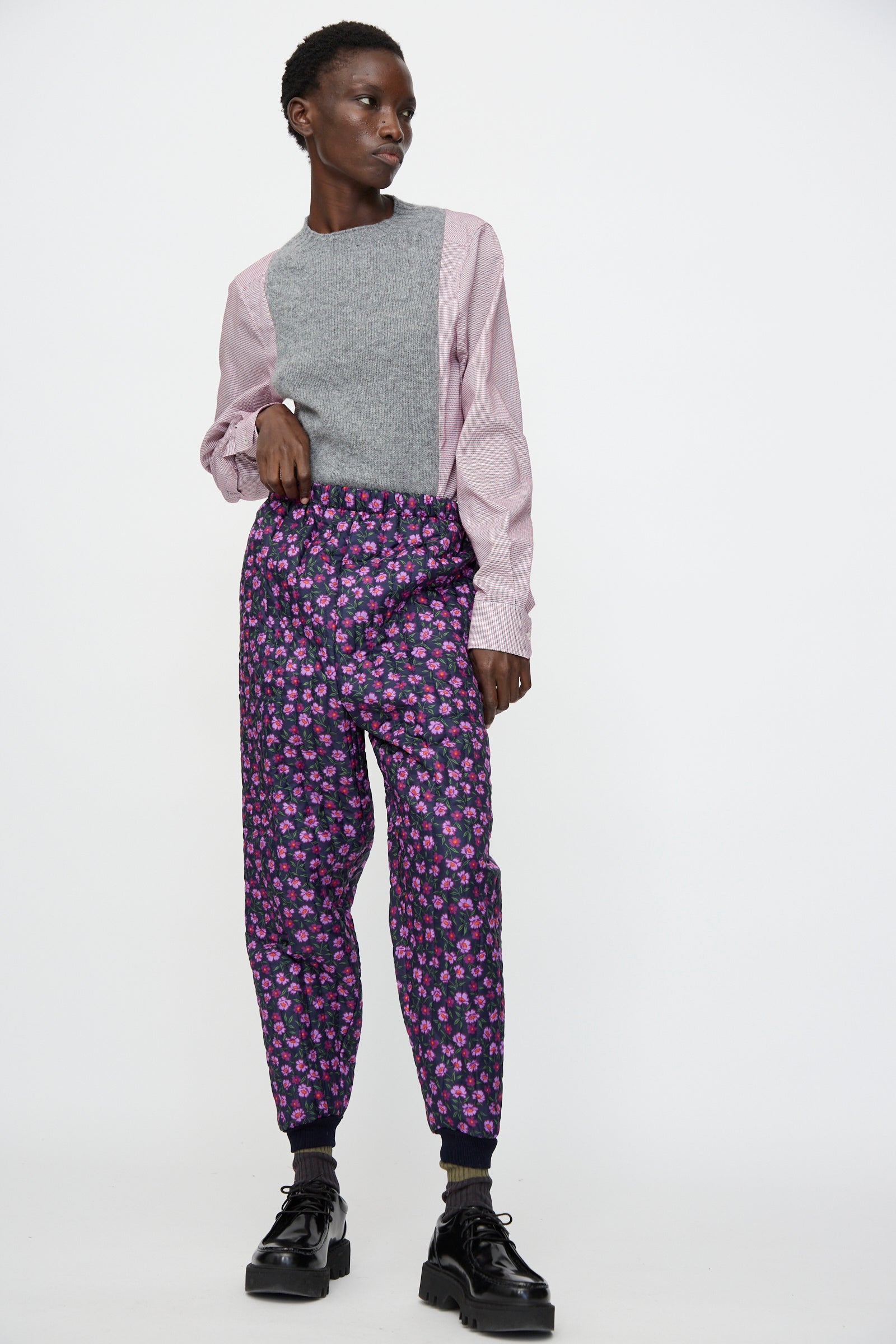A person stands against a plain background wearing a grey and pink long-sleeve top, Bless No. 08 Monpe Pant in Floral Print II, black socks, and black platform shoes.