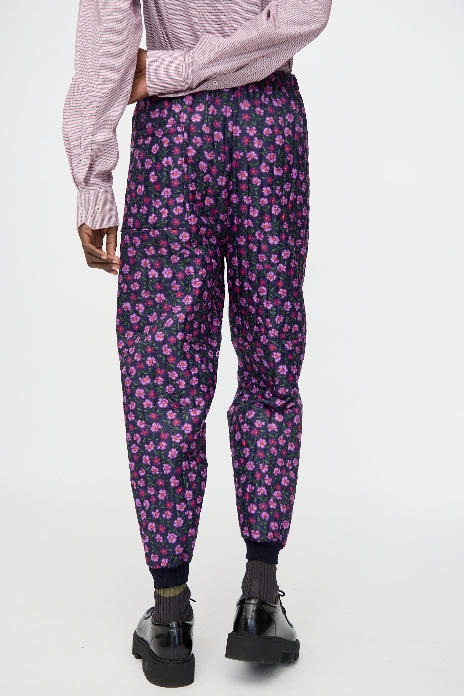A person wearing black shoes and socks, styled in Bless No. 08 Monpe Pant in Floral Print II featuring a pink floral pattern, photographed from the back.