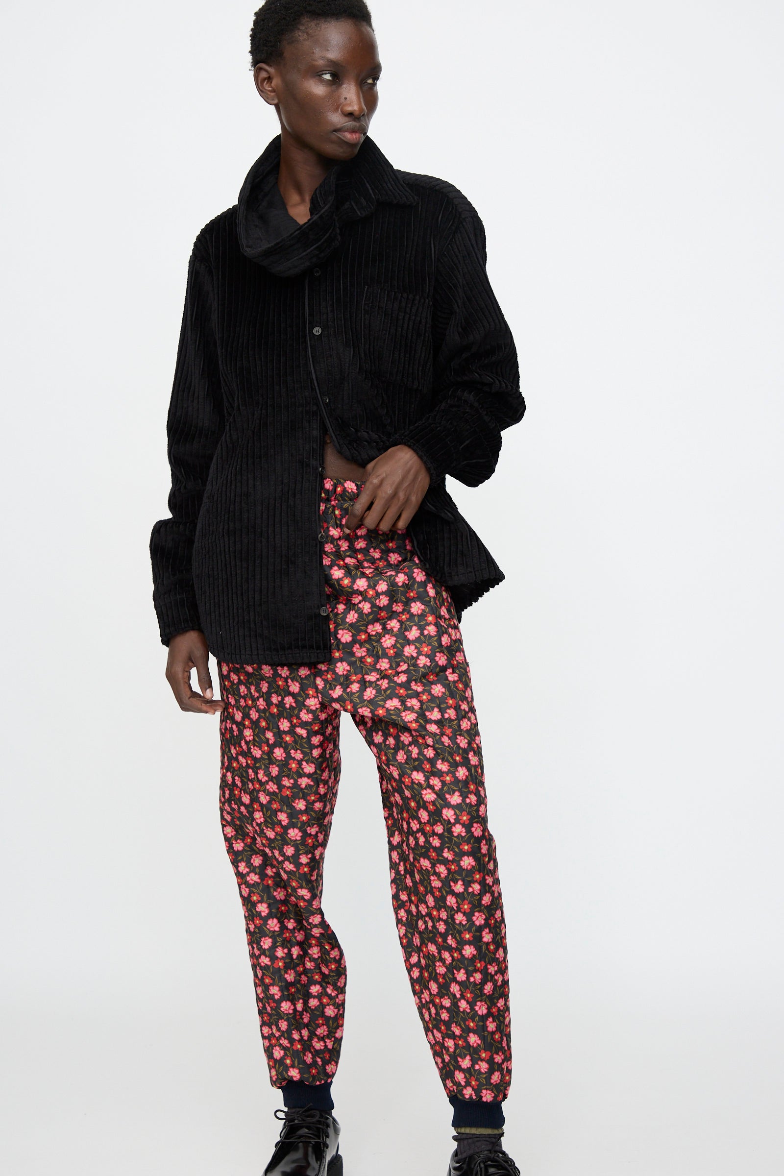 A person wears a black corduroy jacket, black top, and Bless No. 08 Monpe Pant in Floral Print IV, inspired by Japanese workwear, standing against a plain white background.