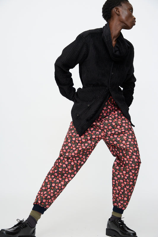 A person models the No. 08 Monpe Pant in Floral Print IV by Bless, paired with a black textured jacket, olive green socks, and black platform shoes against a plain white background.