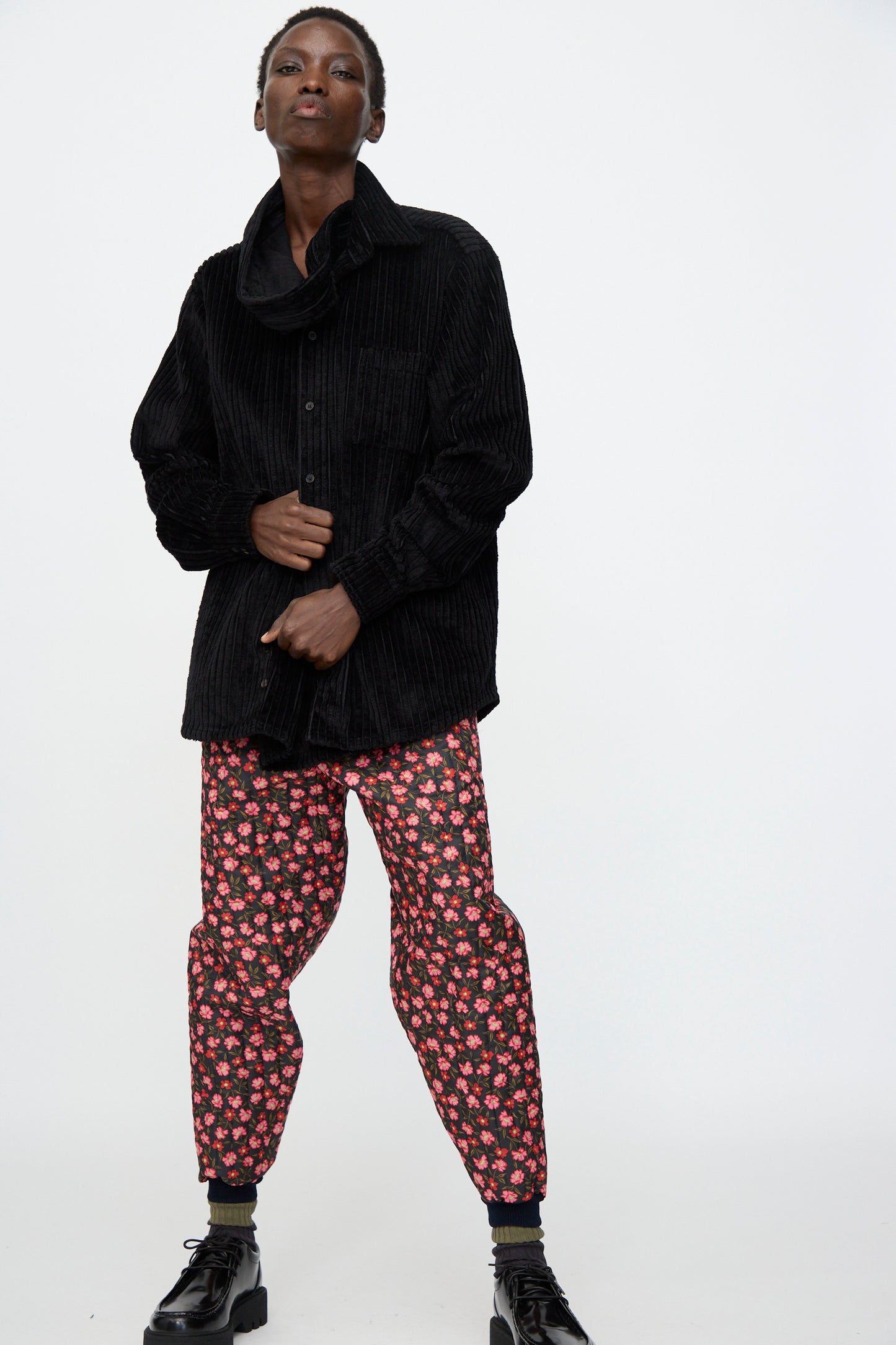 A person wears the Bless No. 08 Monpe Pant in Floral Print IV, a loose black corduroy shirt, and black platform shoes while standing against a plain white background.