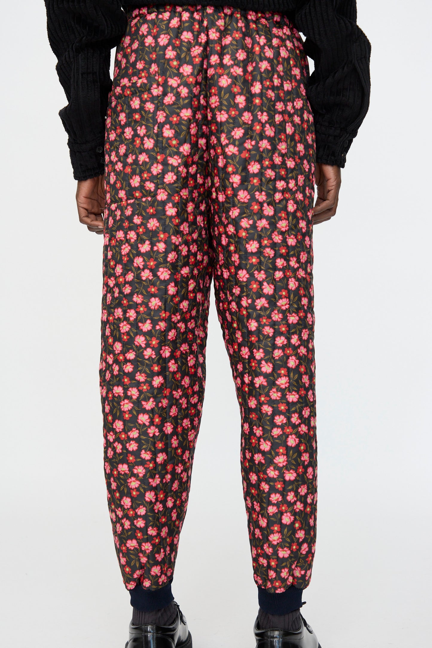 The person is shown from the back wearing Bless No. 08 Monpe Pant in Floral Print IV, featuring a red and pink pattern, paired with black socks and shoes against a plain background.