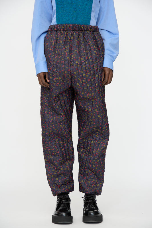 A person wearing a light blue shirt, teal vest, Bless No. 08 Monpe Pant in Floral Print V, and black platform shoes.
